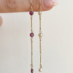 Solstice Earrings displayed side by side in gold, featuring ruby gemstones on one earring and freshwater pearl accents on the other.